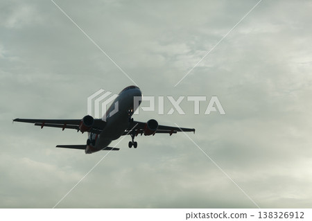 Commercial airplane flying through cloudy sky during sunset, with landing gear deployed and wings extended, capturing the essence of air travel and aviation Commercial airplane flying through cloudy sky during sunset, with landing gear deployed and wings extended, capturing the essence of air travel and aviation 138326912