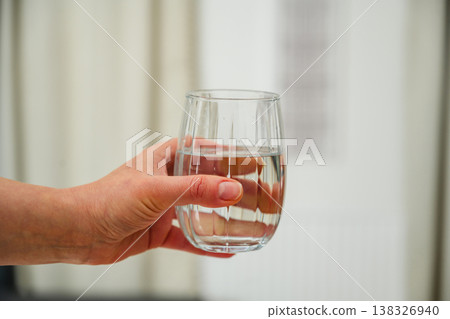 Woman holding a glass of drinking water, hydration, healthy lifestyle. Neutral background 138326940