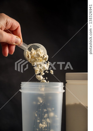 Protein drink. Hand pouring protein powder in a white shaker. Dark background. Body building, muscle growth and food supplement concept 138326941
