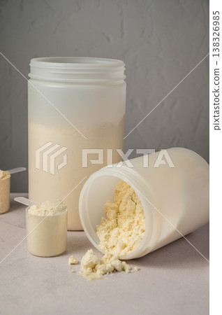 Protein powder in scoops with white plastic protein tubes, jars in background. Body building, muscle growth and food supplement concept Protein powder in scoops with white plastic protein tubes, jars in background. Body building, muscle growth and food supplement concept 138326985