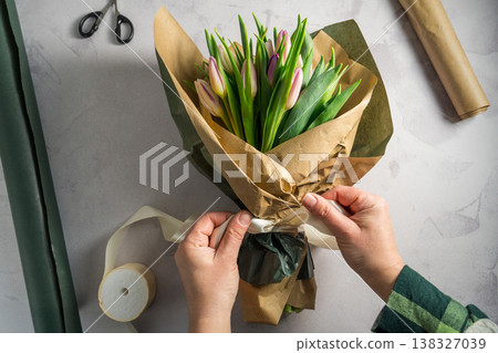 Mother's day, birthday bouquet. Female hands wrapping tulip flowers in craft paper. Spring tulips flower background 138327039