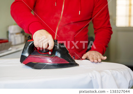 Man's hand ironing clothes on an ironing board at home, copy space Man's hand ironing clothes on an ironing board at home, copy space 138327044