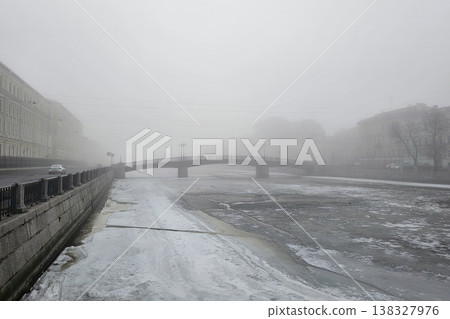 Fog blankets a quiet city street. Lone car glides through misty gloom Fog blankets a quiet city street. Lone car glides through misty gloom 138327976