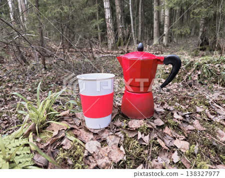 Red coffee maker sits beside a cup on mossy forest floor 138327977