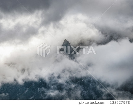 Misty peak rises above swirling clouds 138327978