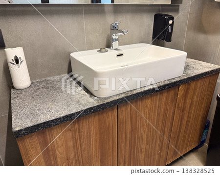 Modern ceramic sink with chrome faucet installed on stone countertop in public restroom interior. Hygiene maintenance, handwashing routine, sanitation infrastructure and facility management concept Modern ceramic sink with chrome faucet installed on stone countertop in public restroom interior. Hygiene maintenance, handwashing routine, sanitation infrastructure and facility management concept 138328525