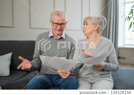 Sad tired disappointed middle aged senior couple sit with paper document. Unhappy older mature man woman reading paper bill managing bank finances calculating taxes planning loan debt pension payment 138329136