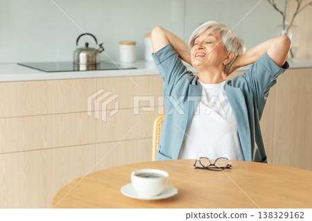 Senior old woman feeling relaxed stretching arms in kitchen at home. Smiling mature woman stretching hands feel positive optimistic fresh on bright morning new day. Good mood happy elderly lifestyle 138329162