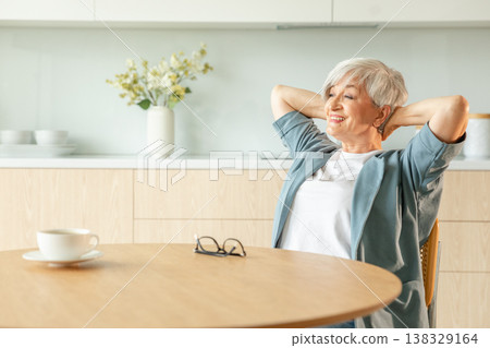 Senior old woman feeling relaxed stretching arms in kitchen at home. Smiling mature woman stretching hands feel positive optimistic fresh on bright morning new day. Good mood happy elderly lifestyle 138329164