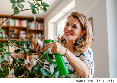 Middle aged woman caring for houseplant at home while practicing mindful self care. Middle aged woman caring for houseplant at home while practicing mindful self care. 138329613