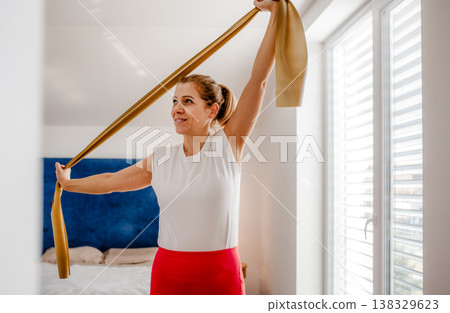 Smiling middle aged woman exercising with resistance band at home. 138329623