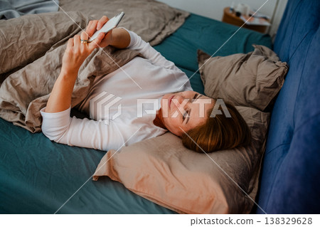Middle aged woman using smartphone while lying in bed at home. 138329628