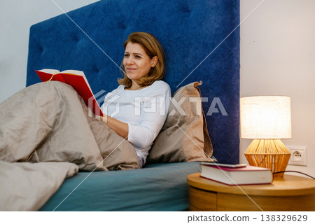 Woman reading book in bed before sleep as healthy evening routine. 138329629