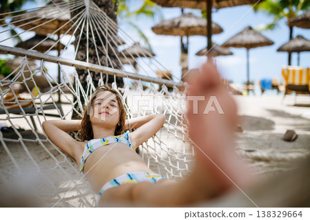 Smiling girl relaxing in hammock during tropical family vacation. Smiling girl relaxing in hammock during tropical family vacation. 138329664