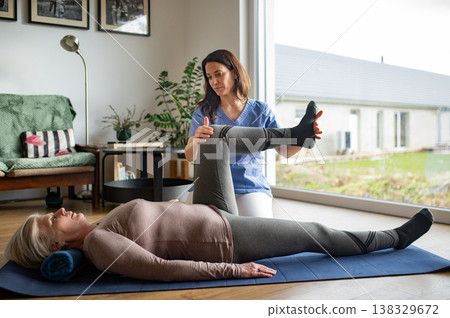 Physiotherapist exercising with older woman during rehabilitation session at home. 138329672