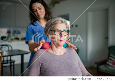Physiotherapist helping senior woman with neck exercise, home therapy session. Physiotherapist helping senior woman with neck exercise, home therapy session. 138329679