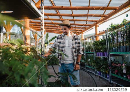 Garden center owner watering plants with hose in greenhouse. 138329739