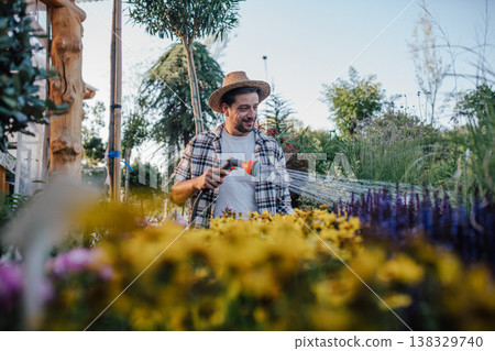 Garden center owner watering plants with hose in greenhouse. Garden center owner watering plants with hose in greenhouse. 138329740