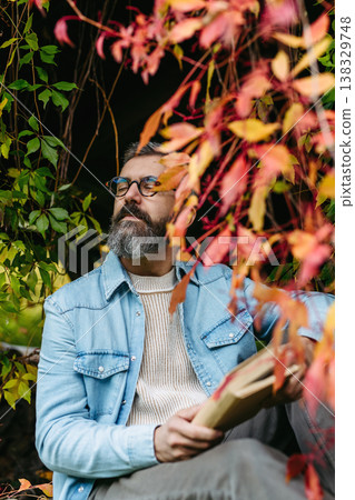 Man is enjoying a relaxing, peaceful moment at home, sitting among greenery and reading a book. Man is enjoying a relaxing, peaceful moment at home, sitting among greenery and reading a book. 138329748