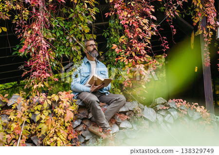 Man is enjoying a relaxing, peaceful moment at home, sitting among greenery and reading a book. Man is enjoying a relaxing, peaceful moment at home, sitting among greenery and reading a book. 138329749