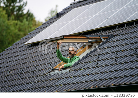 Man looking from skylight, roof window with solar panels above him. Sustainable lifestyle and green household. Man looking from skylight, roof window with solar panels above him. Sustainable lifestyle and green household. 138329750