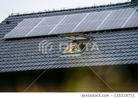 Man looking from skylight, roof window with solar panels above him. Sustainable lifestyle and green household. Man looking from skylight, roof window with solar panels above him. Sustainable lifestyle and green household. 138329751