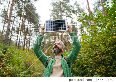 Handsome man standing in the middle of forest, holding small solar panel above his head. Handsome man standing in the middle of forest, holding small solar panel above his head. 138329770