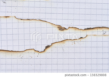 A sheet of white squared notebook paper with a badly burnt top edge and traces of dark soot, close up 138329808