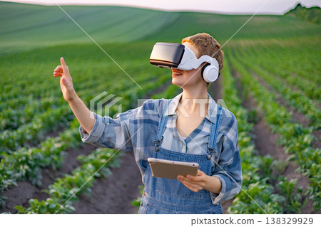 A farmer wearing a virtual reality headset and holding a tablet interacts with technology while standing in a cultivated field A farmer wearing a virtual reality headset and holding a tablet interacts with technology while standing in a cultivated field 138329929