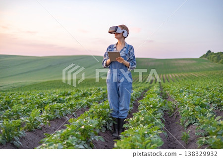 A farmer wearing virtual reality goggles and headphones holds a tablet while standing in a field of crops, embracing agricultural technology A farmer wearing virtual reality goggles and headphones holds a tablet while standing in a field of crops, embracing agricultural technology 138329932
