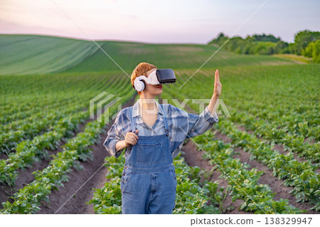 A person wearing a virtual reality headset and headphones stands in a field of crops, gesturing with their hand as they interact with technology 138329947