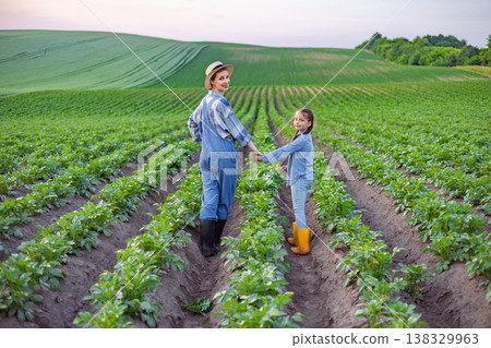 A mother and her young daughter hold hands while walking through rows of crops on a sunny day A mother and her young daughter hold hands while walking through rows of crops on a sunny day 138329963