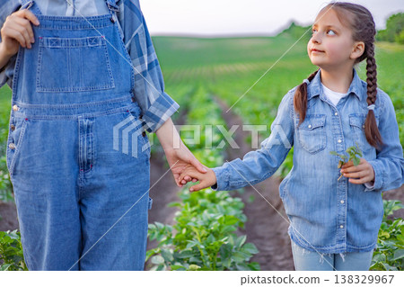 A child and adult hold hands while standing in a lush green field, symbolizing a connection to the land and family heritage A child and adult hold hands while standing in a lush green field, symbolizing a connection to the land and family heritage 138329967
