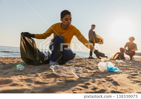 Earth day. Volunteers activists team collects garbage cleaning of beach coastal zone. Woman mans puts plastic trash in garbage bag on ocean shore. Environmental conservation coastal zone cleaning 138330073