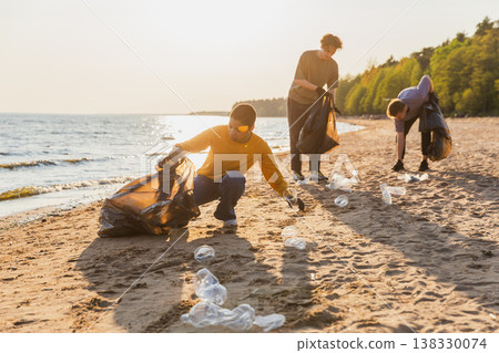Earth day. Volunteers activists team collects garbage cleaning of beach coastal zone. Woman mans puts plastic trash in garbage bag on ocean shore. Environmental conservation coastal zone cleaning Earth day. Volunteers activists team collects garbage cleaning of beach coastal zone. Woman mans puts plastic trash in garbage bag on ocean shore. Environmental conservation coastal zone cleaning 138330074