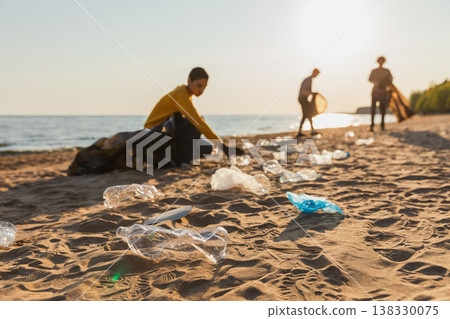 Earth day. Volunteers activists collects garbage cleaning of beach coastal zone. Woman mans with trash in garbage bag on ocean shore. Environmental conservation coastal zone cleaning. Blurred image 138330075