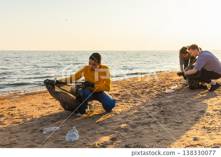 Earth day. Volunteers activists team collects garbage cleaning of beach coastal zone. Woman mans puts plastic trash in garbage bag on ocean shore. Environmental conservation coastal zone cleaning Earth day. Volunteers activists team collects garbage cleaning of beach coastal zone. Woman mans puts plastic trash in garbage bag on ocean shore. Environmental conservation coastal zone cleaning 138330077