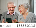 Senior couple man woman shopping online with smartphone paying with credit card. Old people buying on Internet enter credit card details at home indoors. Online shopping delivery service ecommerce 138330118