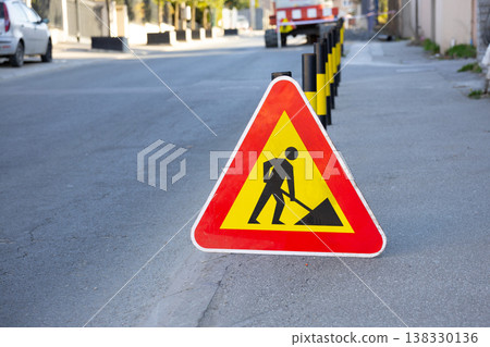 Road work warning sign standing on a residential street. Repair, caution, infrastructure, maintenance, disruption, safety, and temporary traffic control in an everyday urban environment Road work warning sign standing on a residential street. Repair, caution, infrastructure, maintenance, disruption, safety, and temporary traffic control in an everyday urban environment 138330136