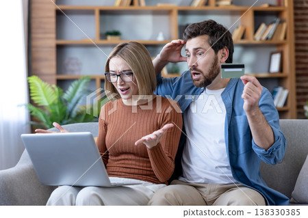 Young couple looking at a laptop with shocked and stressed expressions, holding a credit card and facing financial problems, debt, or a banking error online 138330385