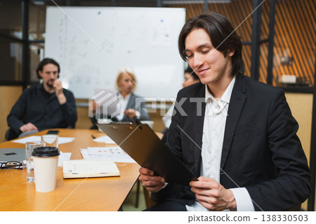 Portrait of team leader businessman in office, colleagues meeting in background. Confident business leader man sitting in office. Boss leader professional worker. Working process office life career 138330503