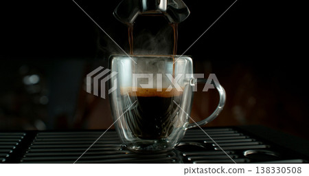 Fresh espresso pouring from coffee machine into glass cup with rich crema and rising steam. Warm cinematic scene capturing preparation of black coffee in cozy atmosphere. 138330508