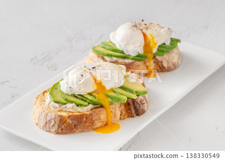 Avocado toast with poached eggs and runny yolk on artisan bread plate Avocado toast with poached eggs and runny yolk on artisan bread plate 138330549