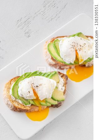 Avocado toast with poached eggs and runny yolk on artisan bread plate 138330551