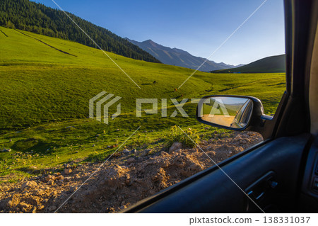 Cows grazing in lush mountain landscape of Kyrgyzstan, driver perspective - view from car Cows grazing in lush mountain landscape of Kyrgyzstan, driver perspective - view from car 138331037