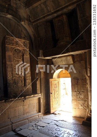 Warm sunlight streams through the open doors of an ancient stone church, illuminating the historic walls and stone floor. 138331692