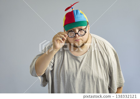 Funny overweight man in propeller cap adjusting glasses, playful comic pose 138332121