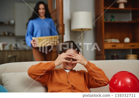 Child playing hide and seek on a sofa while a woman enters with a gift Child playing hide and seek on a sofa while a woman enters with a gift 138332711
