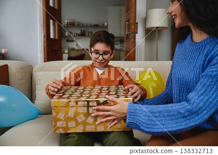 Child opens a beautifully wrapped gift with joy at home during a celebration 138332713