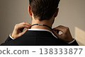 Rear View Of A Man Adjusting Black Necklace Against Blurred Beige Background in Black Suit 138333877